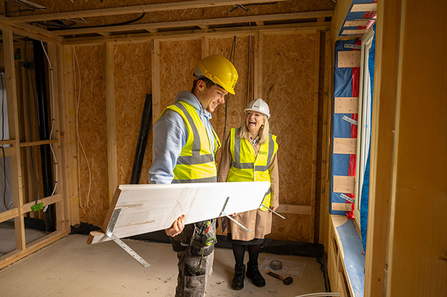 man holding wooden board in building site with woman laughing