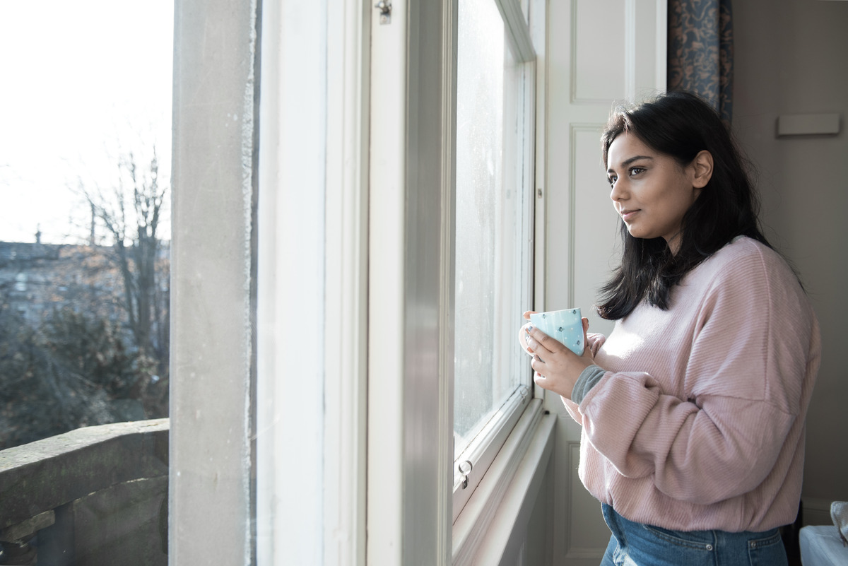 a woman with a cup looking outside her window